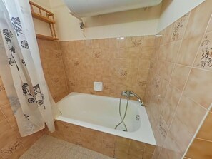 Une salle de bain avec une baignoire, des murs carrelés, un espace douche et des toilettes.
