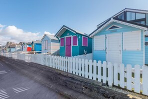 A row of colorful beach huts with white picket fences, each with a door and windows.