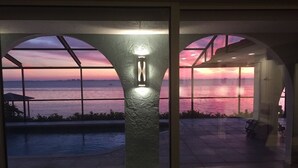 Uima-altaan reunalla on alue, jolta avautuu näkymä auringonlaskuun veden yllä, katettu oleskelualue ja hyvin valaistu pylväs.