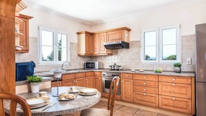 A modern kitchen with wooden cabinets, a granite countertop, and a dining area with a round table and chairs. - Casa del Sol - Six Bedroom Villa, Sleeps 7 (Binibeca)