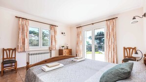 A bedroom with a bed, two chairs, a dresser, a lamp, and a window with curtains. - Casa del Sol - Six Bedroom Villa, Sleeps 7 (Binibeca)