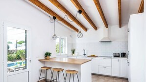 Une cuisine dotée d’un îlot central en bois, de meubles blancs et donnant sur une piscine.