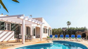 Un espace aménagé au bord de la piscine, comprenant un coin salon couvert, une piscine et un panier de basketball.