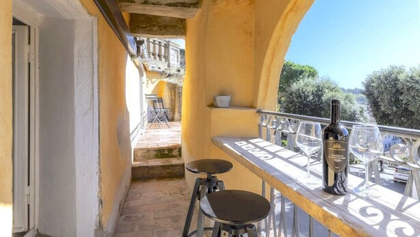 Ein Balkon mit Tisch, zwei Hocker, einer Weinflasche und Gläsern.