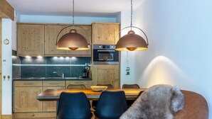 A modern kitchen with wooden cabinets, a dining table with chairs, and pendant lighting.