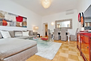 Uma sala de estar moderna com um sofá, uma mesa de centro de vidro e uma área de jantar com cadeiras e uma mesa.