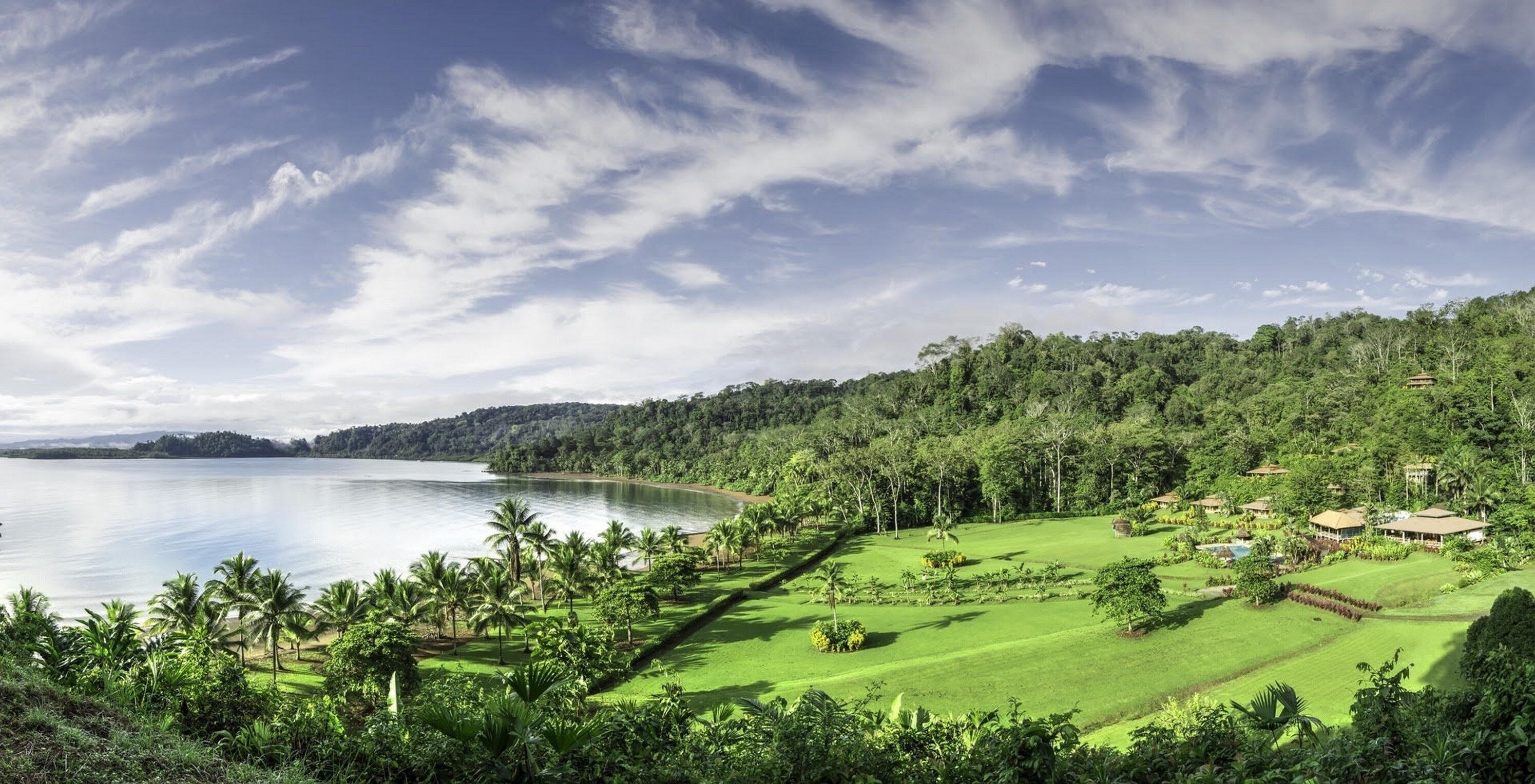A coastal landscape with a golf course, lush greenery, and a body of water.