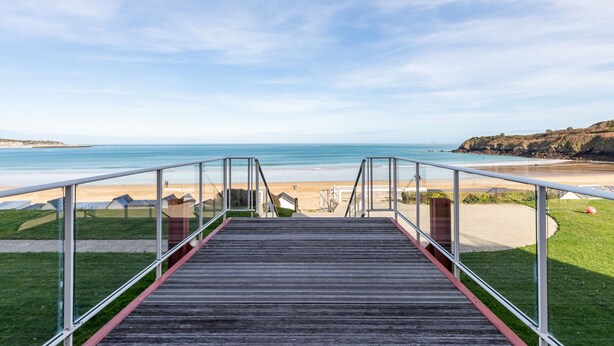 Un escalier en bois mène à une plage d’où l’on a une vue dégagée sur l’océan et les collines lointaines.