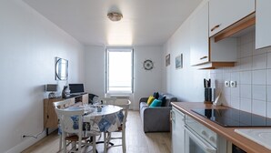 Une cuisine moderne avec des meubles blancs, un coin repas comprenant une table et des chaises, et un canapé gris.