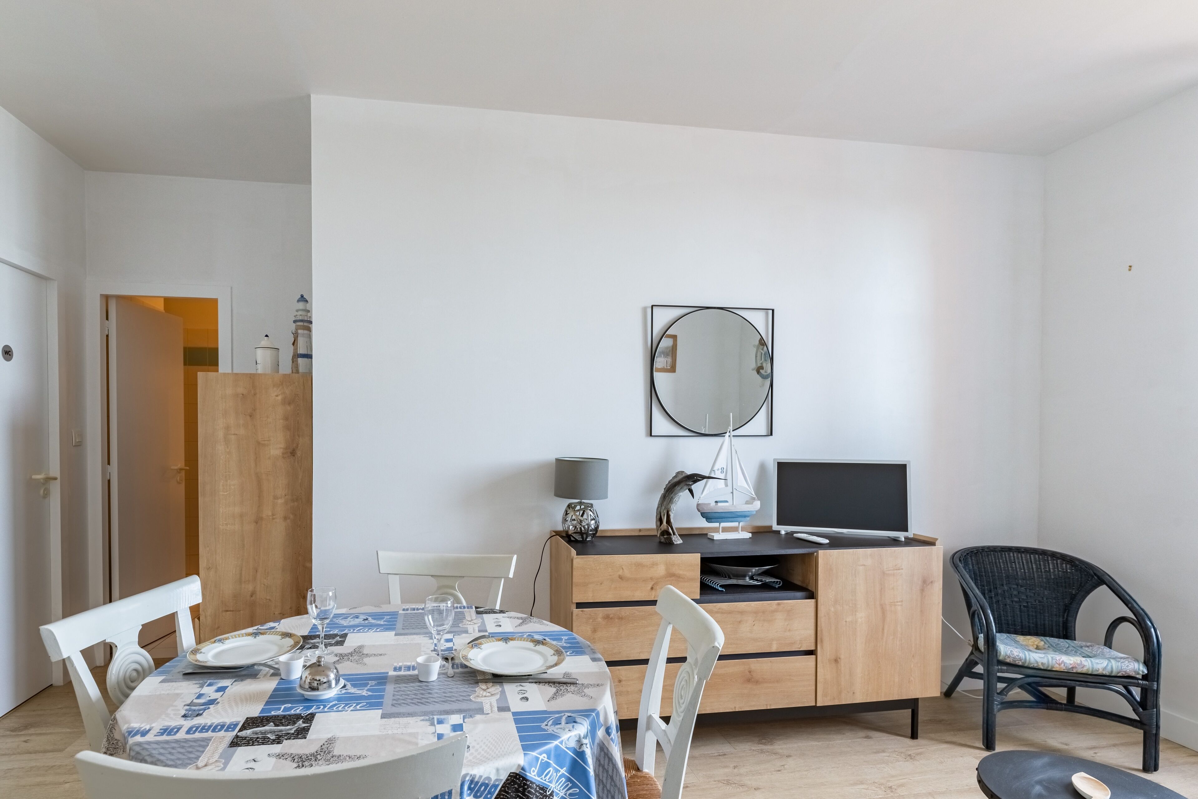 Un coin repas avec une table dressée pour quatre personnes, un meuble en bois, une chaise noire et un téléviseur posé sur un support en bois.