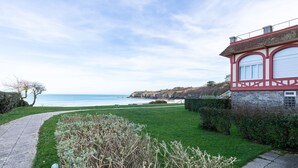Une propriété située sur la côte, avec un chemin pavé menant à une zone herbeuse et un bâtiment en pierre doté de grandes fenêtres.