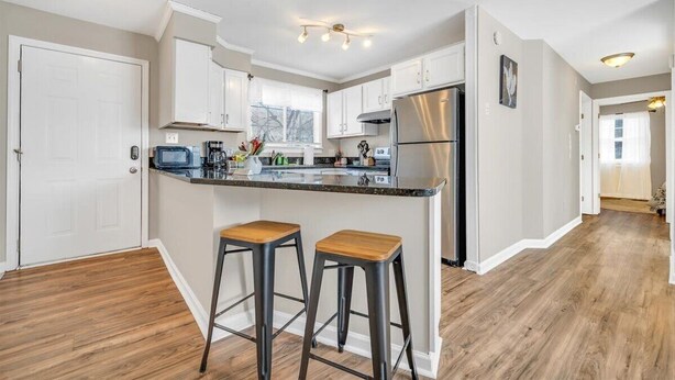 Una cocina moderna con armarios blancos, un refrigerador de acero inoxidable y una isla de madera con taburetes.