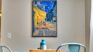 Un comedor con una mesa y sillas, un cuadro en la pared y un florero sobre la mesa.