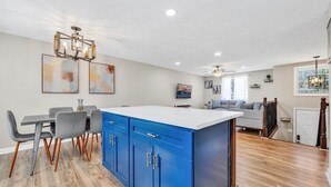 Una cocina moderna con armarios azules, una isla blanca y un comedor con sillas grises.