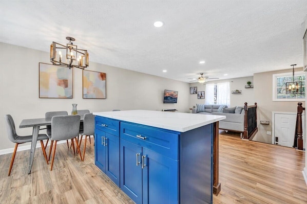 A modern kitchen with blue cabinets, a white island, and a dining area with grey chairs.