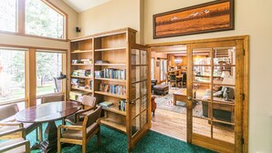 A spacious reading room with large windows, wooden bookshelves, and a comfortable seating area. - A Lovely home, Pet Friendly, Hot Tub & National Forest (Black Butte Ranch)