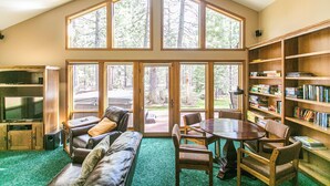 A spacious living area with a large window, a fireplace, a bookshelf, and a television. - A Lovely home, Pet Friendly, Hot Tub & National Forest (Black Butte Ranch)