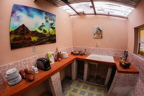 Una cocina compacta con un lavamanos, un tostador y un cuadro de un paisaje.