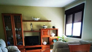 A living room with a sofa, a TV, wooden cabinets, and a dining table with chairs. - Cottage (Vilaboa)