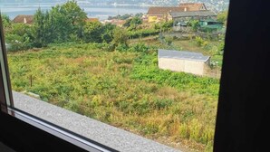 A view from a window overlooking a grassy area with a building and distant mountains. - Cottage (Vilaboa)