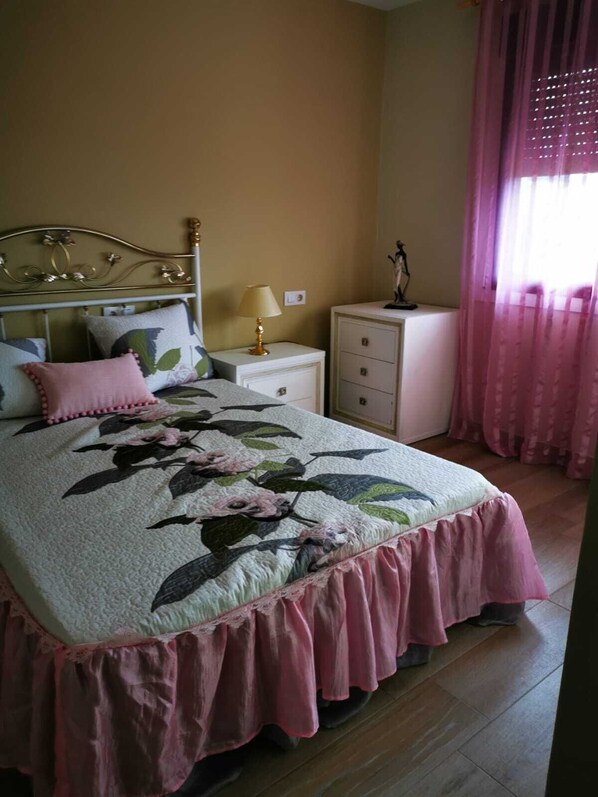 A bedroom with a bed, a nightstand, a dresser, and a window with curtains.