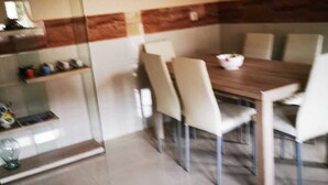 A dining area with a wooden table and six chairs. There is a glass partition with shelves on the left. - Cottage (Vilaboa)