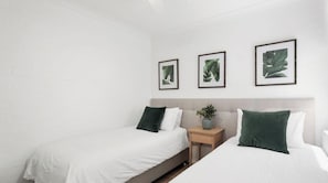 Une chambre d’hôtel avec deux lits, une table de chevet ornée d’une plante et des œuvres d’art représentant des feuilles, encadrées et accrochées au mur.