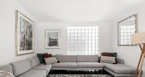 Un salon moderne avec un canapé d’angle, une grande fenêtre à vitraux décoratifs et des œuvres d’art encadrées accrochées aux murs.