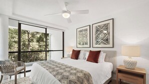 A bedroom with a large bed, a chair, a nightstand, a ceiling fan, and two framed artworks.