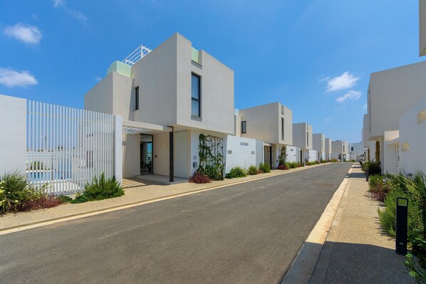 A modern residential street with contemporary houses, a clear sky, and a sidewalk. - Protaras Almaria Villa 16 (Protaras)
