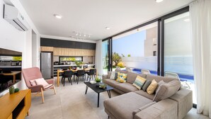 A modern living room with a sofa, armchair, and dining area. - Protaras Almaria Villa 16 (Protaras)