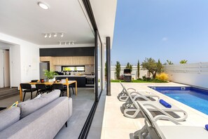 A modern kitchen with a dining area, a poolside lounge, and a view of the pool. - Protaras Almaria Villa 16 (Protaras)