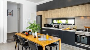 A modern kitchen with dark cabinets, a wooden countertop, and a built-in oven. There is a dining area with a wooden table and black chairs. - Protaras Almaria Villa 16 (Protaras)