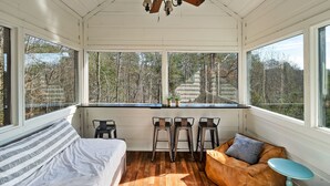 A room with a bed, a desk with three chairs, a ceiling fan, and large windows with a view of trees. - ⛰Mtn Views, 🔥Fire Pit, Hot Tub, 🕹Game/Movie Room (Sevierville)