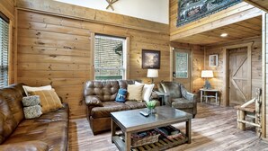 A cozy cabin interior with wooden walls, a leather sofa, a coffee table, and a rustic decor. - ⛰Mtn Views, 🔥Fire Pit, Hot Tub, 🕹Game/Movie Room (Sevierville)