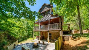 A cabin with a stone exterior, a wooden deck, and a fire pit area. - ⛰Mtn Views, 🔥Fire Pit, Hot Tub, 🕹Game/Movie Room (Sevierville)