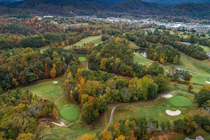 Vista aérea de un campo de golf con múltiples áreas verdes, búnkeres de arena y un entorno boscoso.