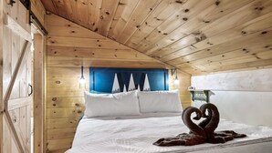 A wooden cabin bedroom with a bed, pillows, and a wall-mounted light fixture. - ⛰Mtn Views, 🔥Fire Pit, Hot Tub, 🕹Game/Movie Room (Sevierville)