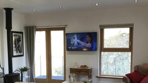 A living room with a beige sofa, a television on the wall, and a window with a view of trees. - Luxurious Studio Apartment in Fahan, Co Donegal (Fahan)