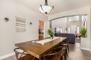 Un vaste espace de salle à manger avec une table et des chaises en bois, un luminaire suspendu et une vue sur la cuisine et le salon.