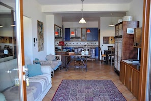 Una sala de estar acogedora con un sofá, una mesa de centro y una alfombra. Al fondo, se observa una cocina con una mesa de comedor y sillas.