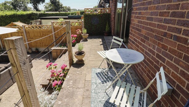 A patio area with a table and chairs, a wooden fence, potted plants, and a brick wall. - Hillcrest (Wrexham)