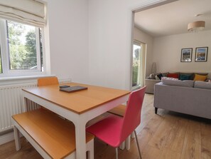 Uma sala de estar moderna com área de jantar, apresentando uma mesa de madeira, uma cadeira vermelha, um sofá cinza e um candelabro.
