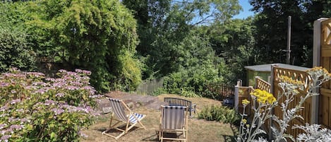 A backyard with two striped lawn chairs, a wooden fence, and various plants.
