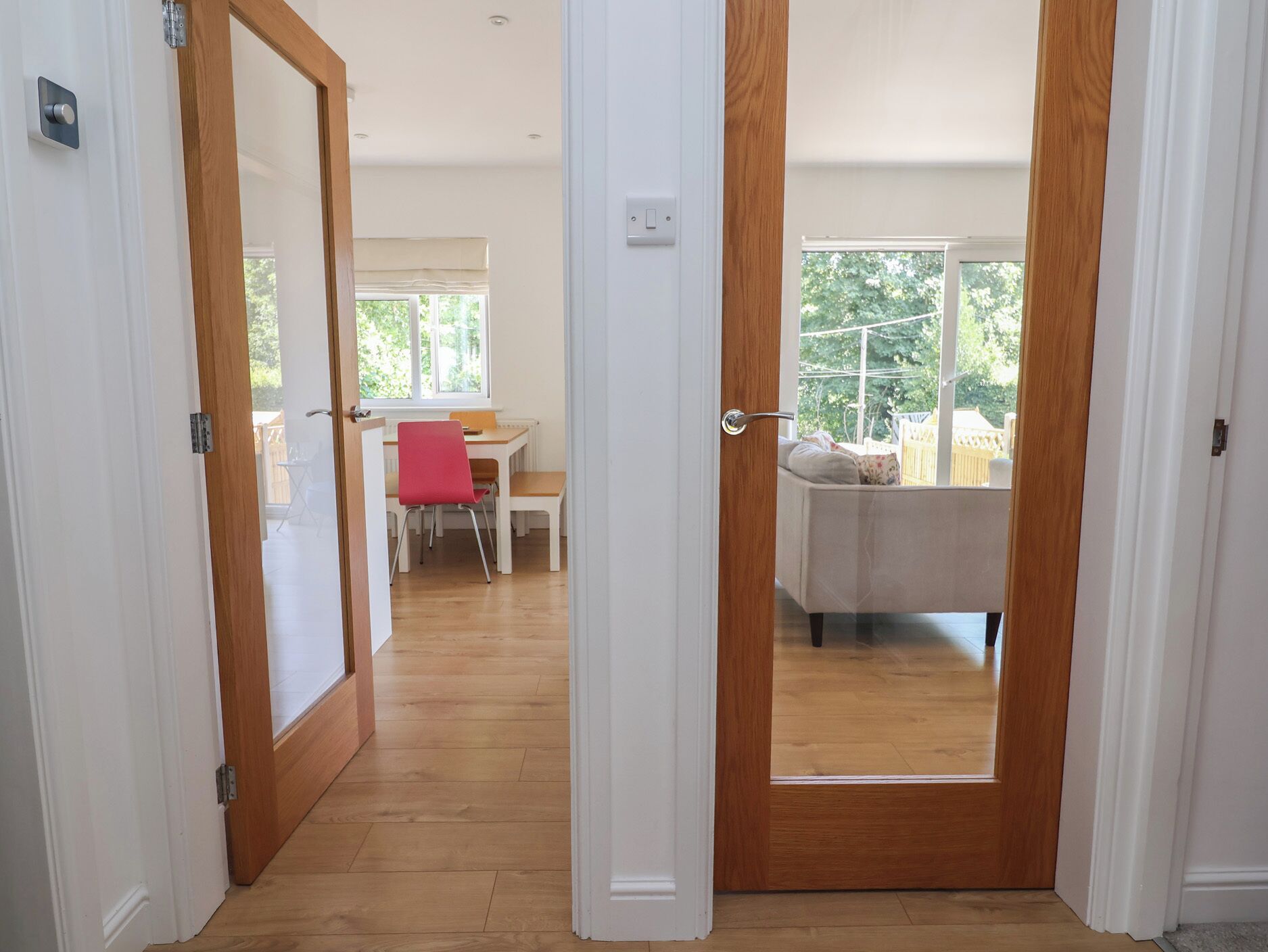 A hallway leading to a room with a window, a wooden floor, and a door with a handle.