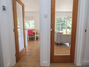 A hallway leading to a room with a window, a wooden floor, and a door with a handle. - Hillcrest (Wrexham)