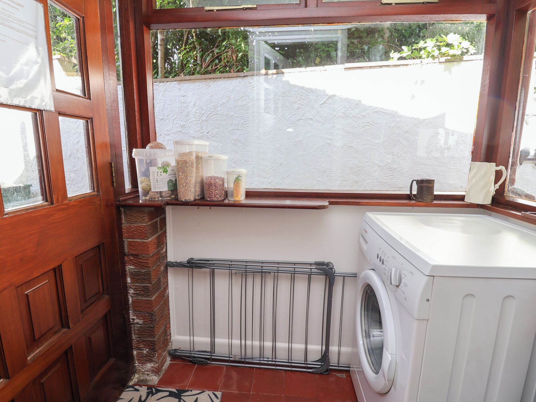 A compact laundry room with a washing machine, a radiator, and storage containers on a shelf.