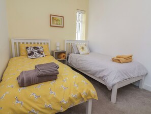 A bedroom with two single beds, each with a distinct patterned bedspread, a bedside lamp, and a small shelf with a cushion. - Hillcrest (Wrexham)