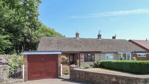 A two-story house with a red garage door, a brick driveway, and a well-maintained garden. - Hillcrest (Wrexham)