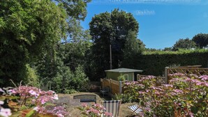 A garden with a small wooden structure, a bench, and various plants. - Hillcrest (Wrexham)